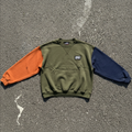 Colorblock Crew sweatshirt in olive, orange, and navy, flat lay on concrete